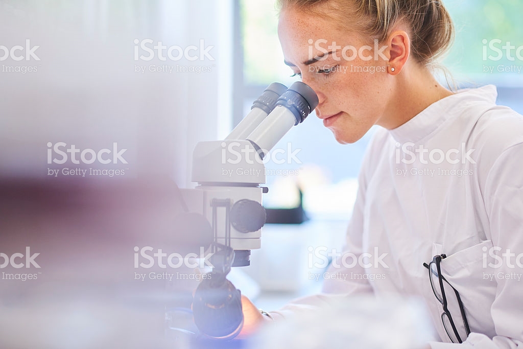 Girl with white coat looking in a microscope